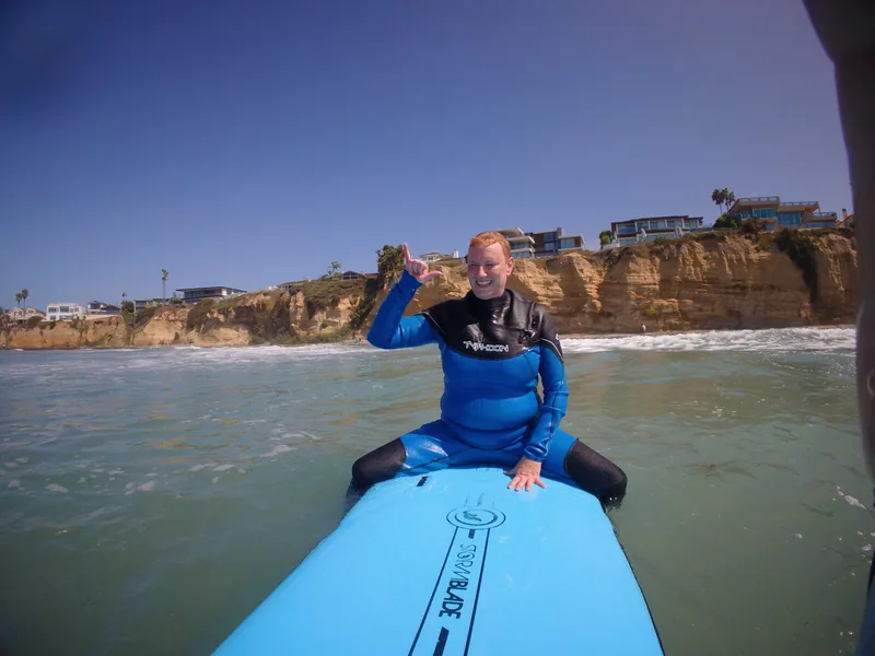 A smiling surfer sitting on a blue board in the shallows
