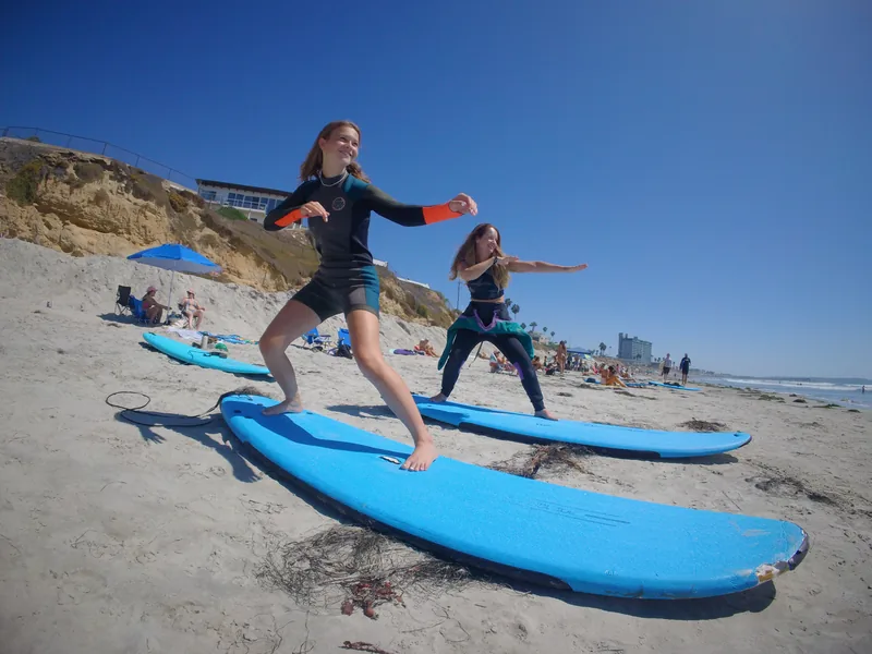 Two surfers practicing their stance on blue surfboards on the sand