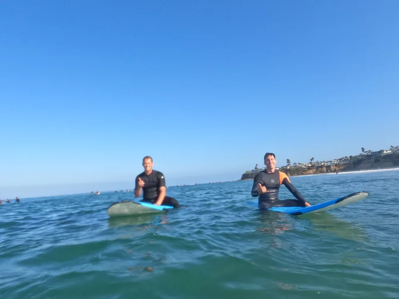 Two surfers sitting on boards in the water under a blue sky